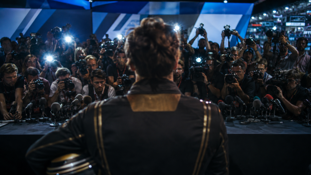 Formula One driver faces a packed press conference as cameras flash and microphones crowd the podium.